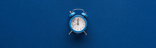 top view of alarm clock on blue background, panoramic shot