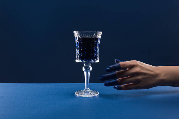 обрезанный вид женской руки с раскрашенными пальцами возле огранённого стекла с напитком, изолированным на голубом
