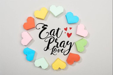 Top view of frame of colorful paper hearts on grey background with eat, pray, love illustration