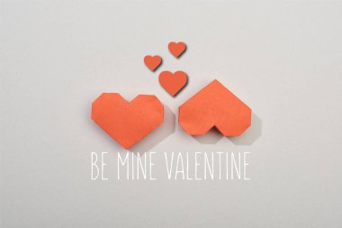 Top view of two red paper hearts on grey background with be mine valentine lettering
