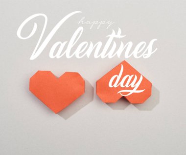Top view of two red paper hearts on grey background with happy valentines day lettering