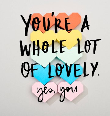 Top view of colorful heart shaped papers on grey background with you are a whole lot of lovely lettering