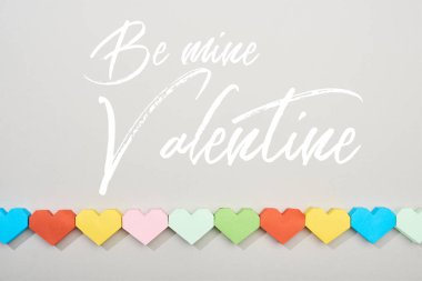 Top view of decorative papers in heart shape on grey background with be mine valentine lettering