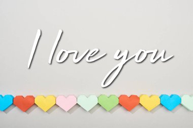 Top view of decorative papers in heart shape on grey background with i love you lettering