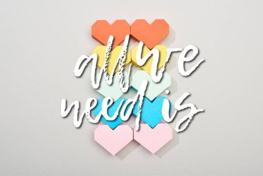 Top view of colorful paper hearts on grey background with all we need is lettering