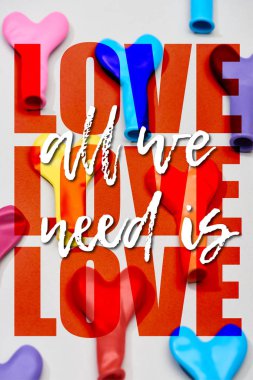 Top view of colorful balloons in heart shape on grey background with all we need is love illustration