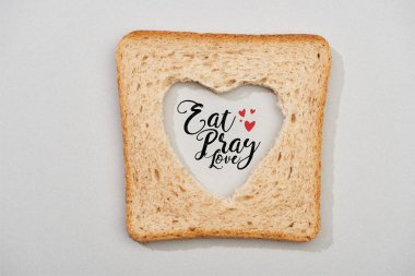 Top view of bread slice with carved heart and eat, pray, love lettering on grey background