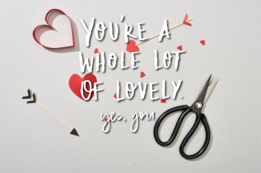 Top view of heart shaped papers with arrows and scissors on grey background with you are a whole lot of lovely lettering