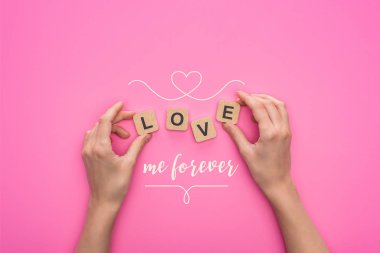 partial view of woman holding cubes with love me forever lettering on pink background clipart