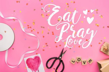 top view of valentines confetti, empty compact disk, scissors, gift boxes, greeting card and love lettering on wooden cubes on pink background with eat, pray, love lettering clipart