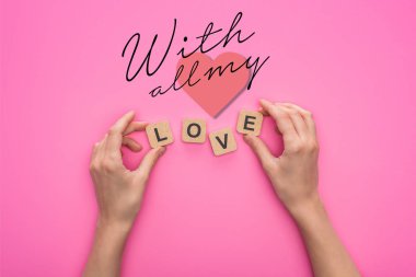 Pembe arka planda aşk yazıları olan küpleri tutan kadının kısmi görüntüsü.