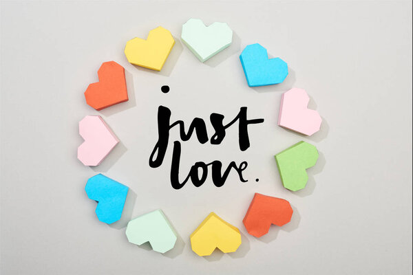Top view of frame of colorful paper hearts on grey background with just love lettering