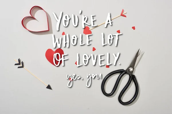 Top view of heart shaped papers with arrows and scissors on grey background with you are a whole lot of lovely lettering