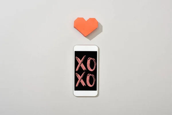 灰色の背景にXoxoイラストと紙の心を持つスマートフォンのトップビュー — ストック写真