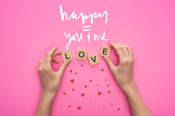 partial view of woman holding cubes with love lettering on pink background with happy you and me illustration