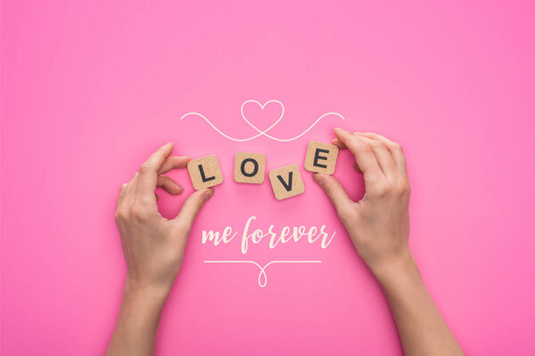 partial view of woman holding cubes with love me forever lettering on pink background