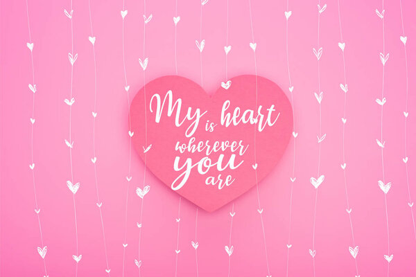 top view of paper heart with my heart is wherever you are lettering isolated on pink