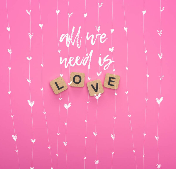 top view of love lettering on wooden cubes on pink background with all you need is love illustration
