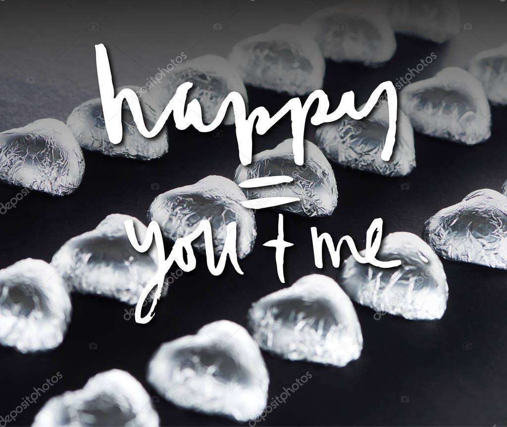 Heart shaped candies in foil on black background with happy you and me lettering