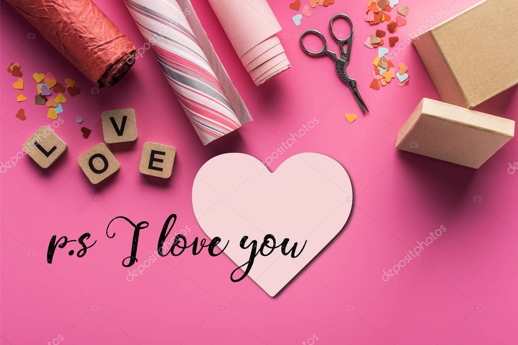 Top view of valentines decoration, scissors, gift box, wrapping paper and love lettering on wooden cubes on pink background with heart and ps i love you lettering