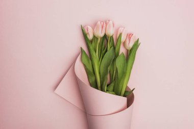 top view of tulips wrapped in paper on pink background