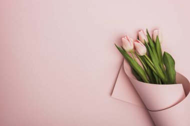 top view of tulips wrapped in paper on pink background