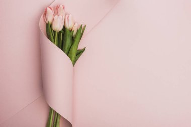 top view of tulip bouquet wrapped in paper swirl on pink background