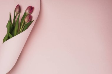 top view of purple tulips wrapped in paper swirl on pink background