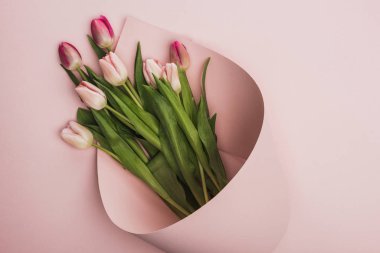 top view of pink and purple tulips wrapped in paper swirl on pink background