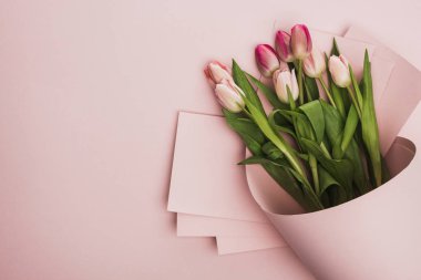 top view of pink and purple tulips wrapped in paper swirl on pink background