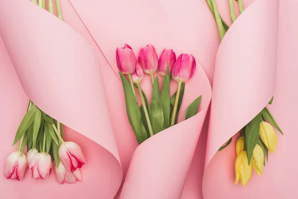 Вид Сверху Розовых Желтых Тюльпанов Завернутых Бумажные Спирали Розовом Фоне — стоковое фото