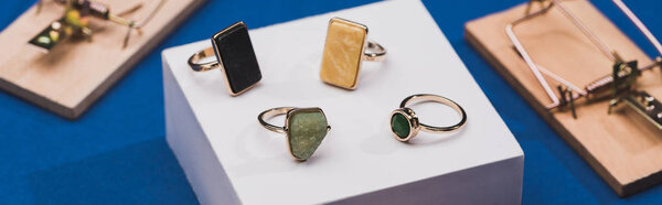 Крупный план ювелирных колец на белом кубе с мышеловками на синем фоне, панорамный снимок
