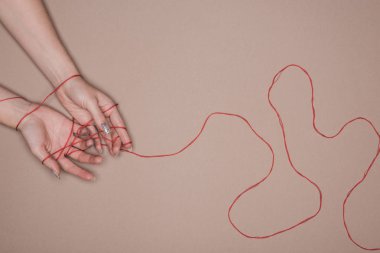 Top view of female hands wrapped in red string on beige background clipart