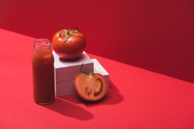 Kırmızı zemin üzerinde olgun domateslerin yanında cam şişede taze sebze suyu.