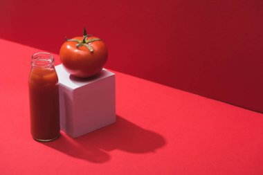 Cam şişede taze sebze suyu ve kırmızı zemin üzerinde olgun domates.