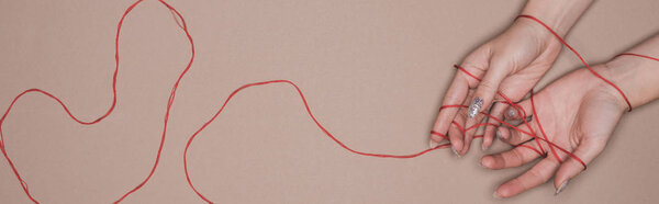 Top view of female hands with red string on beige background, panoramic shot