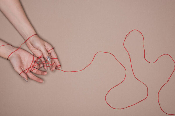Top view of female hands wrapped in red string on beige background