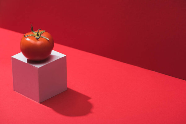 fresh ripe tomato on cube on red background