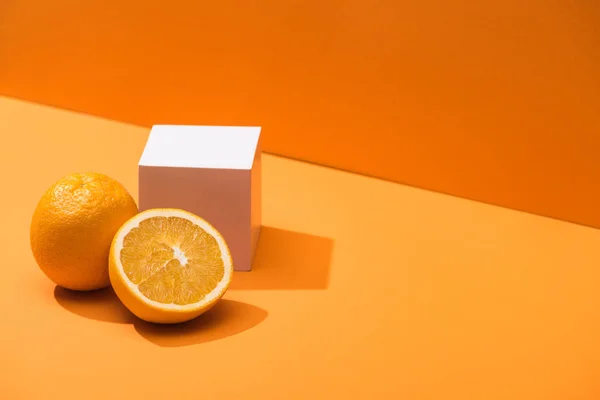 fresh oranges and white cube on orange background