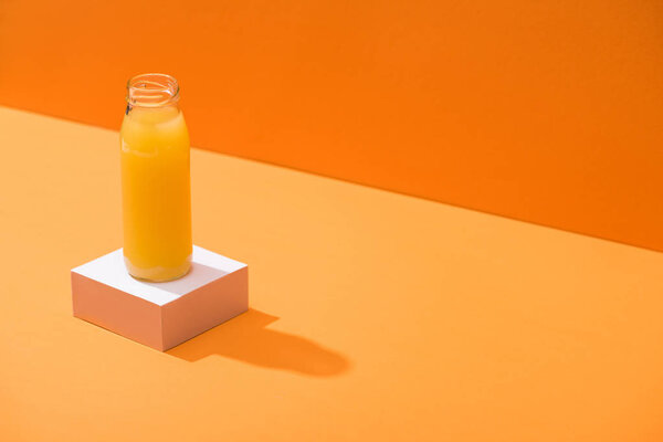 fresh juice in glass bottle on white cube on orange background