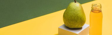 fresh juice in bottle near pear and white cube on green and yellow background, panoramic shot