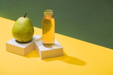 fresh juice in bottle near pear and white cubes on green and yellow background