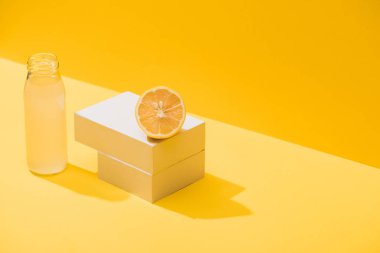 fresh juice in bottle near lemon and white cubes on yellow background