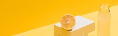 fresh juice in bottle near lemon and white cubes on yellow background, panoramic shot