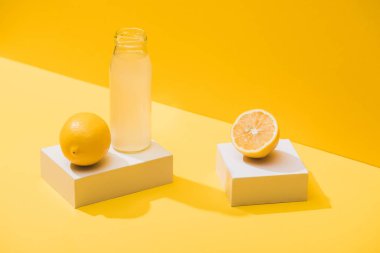 fresh juice in bottle near lemons and white cubes on yellow background
