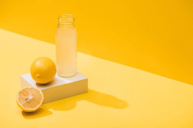 fresh juice in bottle near lemons and white cube on yellow background clipart