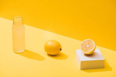 fresh juice in bottle near lemons and white cube on yellow background