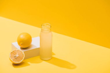fresh juice in bottle near lemons and white cube on yellow background