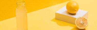 fresh juice in bottle near lemons and white cube on yellow background, panoramic shot