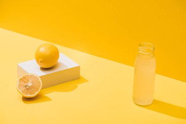 fresh juice in bottle near lemons and white cube on yellow background